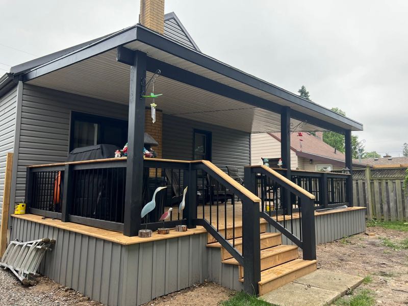 Covered porch with black posts and railings, wood decking and stairs