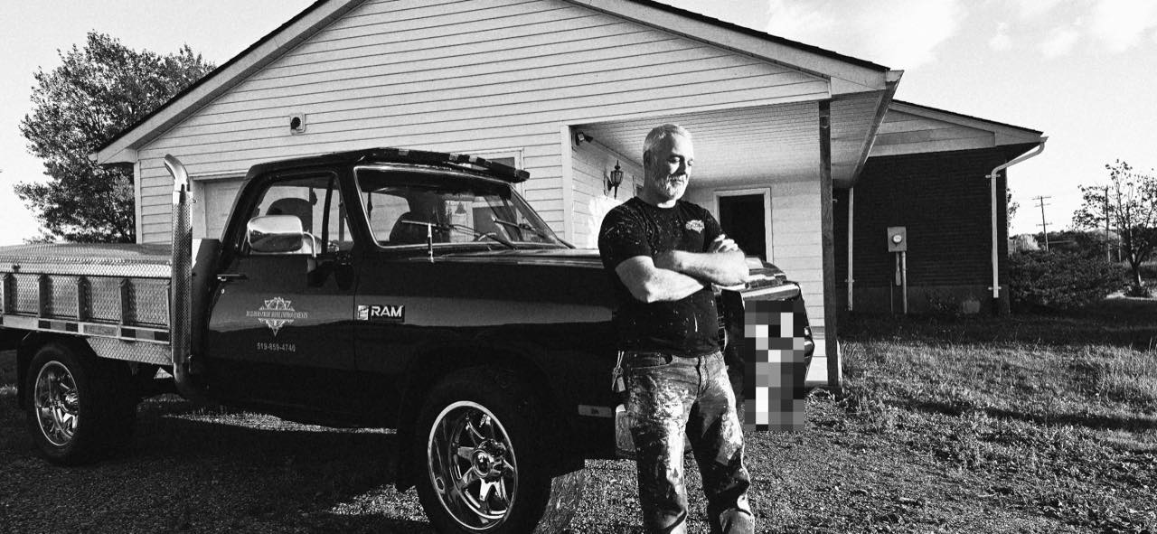 The owner leaning on the Builders Pride flatbed truck, with the company lettering and phone number on the door